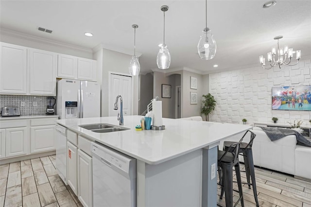 kitchen with sink, hanging light fixtures, a center island with sink, white appliances, and white cabinets