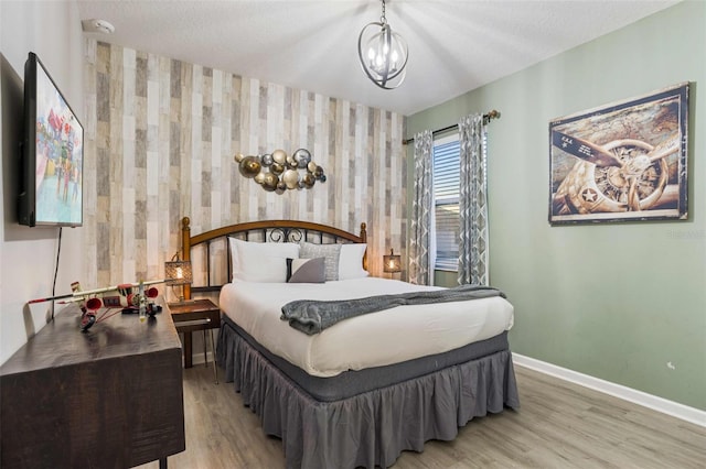 bedroom with light hardwood / wood-style floors, a textured ceiling, and a notable chandelier