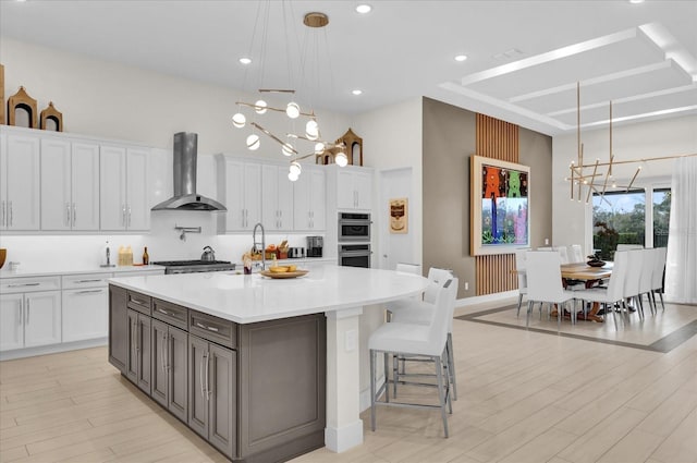 kitchen with pendant lighting, white cabinets, a large island, an inviting chandelier, and wall chimney exhaust hood