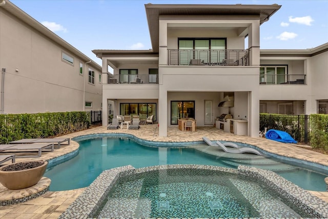 rear view of house with a swimming pool with hot tub, a patio, a balcony, and area for grilling