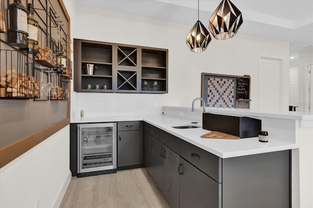 kitchen featuring sink, kitchen peninsula, pendant lighting, beverage cooler, and light hardwood / wood-style floors