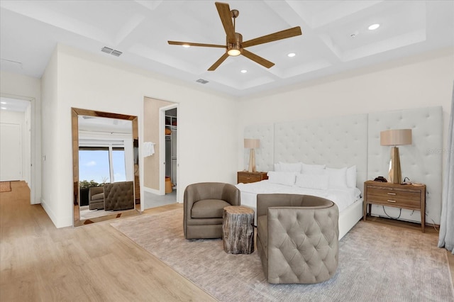 bedroom with ceiling fan, coffered ceiling, light wood-type flooring, and a spacious closet