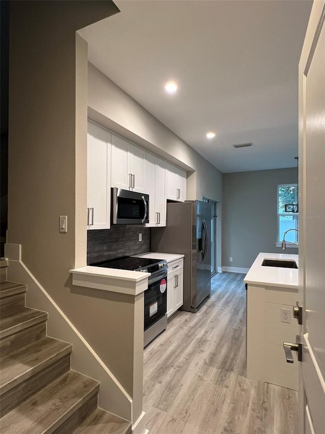 kitchen with appliances with stainless steel finishes, sink, white cabinets, kitchen peninsula, and light wood-type flooring