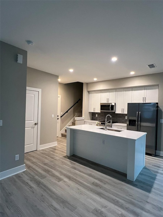 kitchen with black fridge with ice dispenser, sink, an island with sink, decorative backsplash, and white cabinets