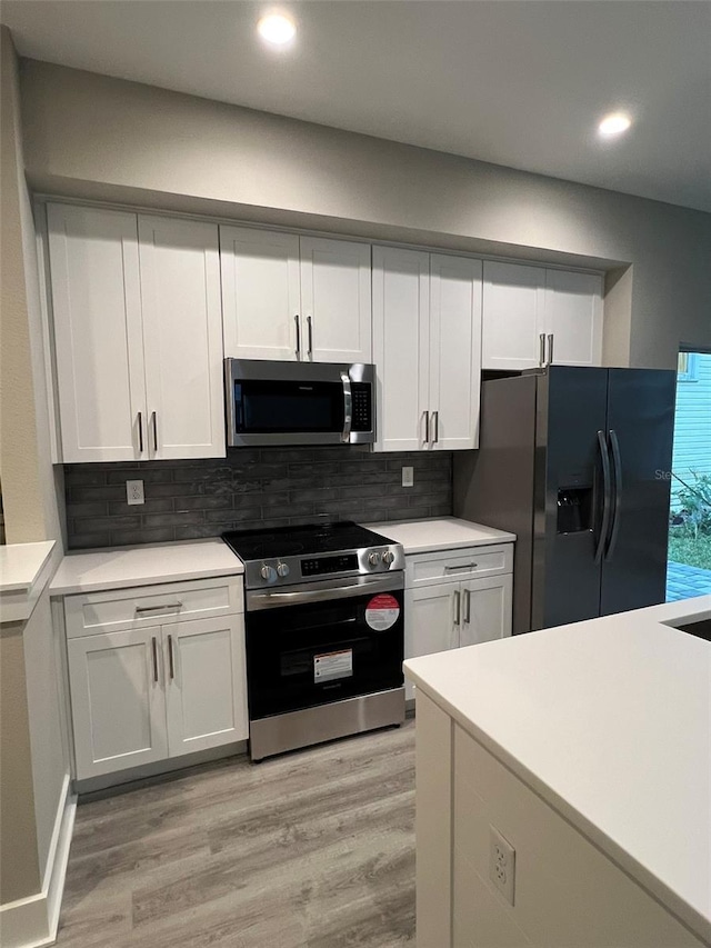 kitchen with backsplash, appliances with stainless steel finishes, light hardwood / wood-style floors, and white cabinets