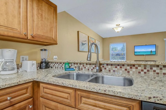 kitchen with tasteful backsplash, light stone countertops, and sink