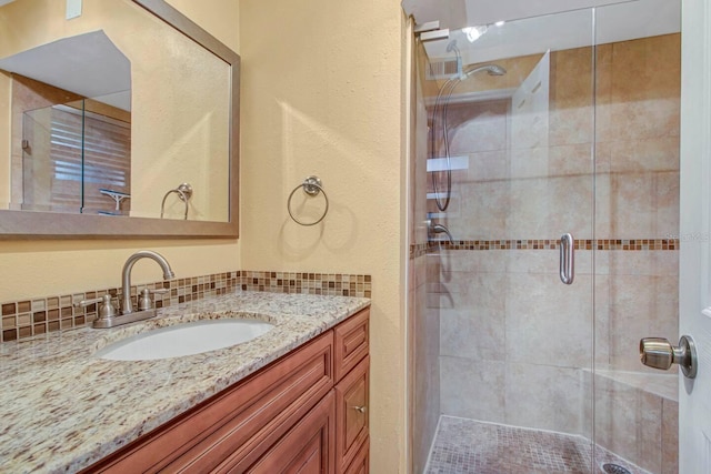 bathroom with vanity, a shower with shower door, and decorative backsplash