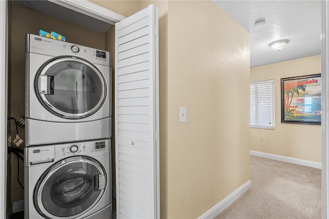 clothes washing area with a textured ceiling, light colored carpet, stacked washer and dryer, laundry area, and baseboards