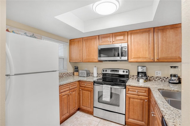 kitchen with light stone counters, a tray ceiling, stainless steel appliances, light tile patterned flooring, and a sink