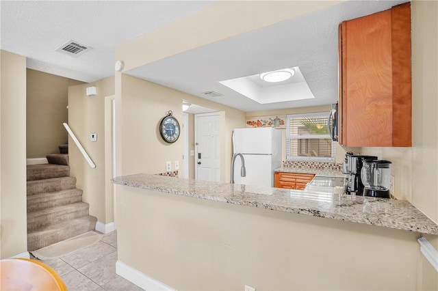 kitchen with light tile patterned floors, light stone counters, a peninsula, visible vents, and freestanding refrigerator