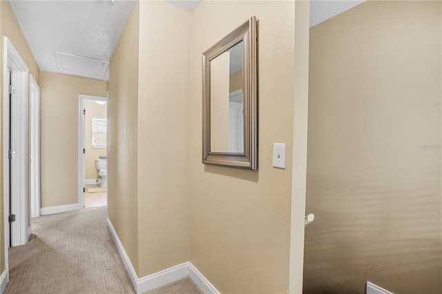 hall featuring baseboards, attic access, and light colored carpet