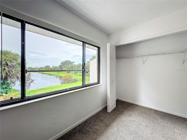 unfurnished bedroom featuring a closet, carpet floors, a water view, and a textured ceiling