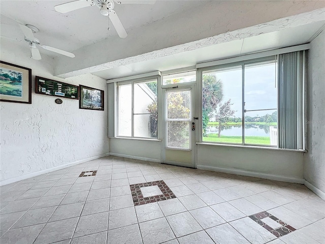 tiled empty room featuring ceiling fan and a water view