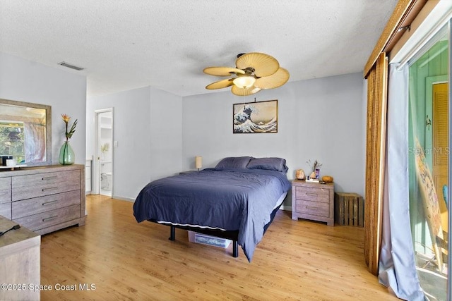 bedroom with light wood-type flooring, ceiling fan, connected bathroom, and a textured ceiling