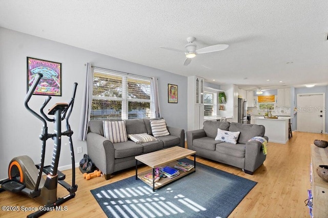 living room with ceiling fan, a textured ceiling, and light hardwood / wood-style flooring