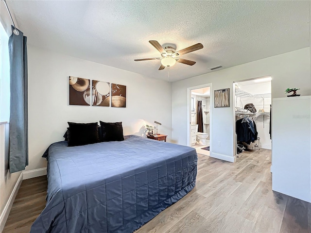 bedroom with connected bathroom, a closet, a walk in closet, ceiling fan, and light hardwood / wood-style flooring