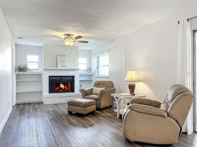 living room featuring ceiling fan, hardwood / wood-style flooring, a fireplace, and a textured ceiling