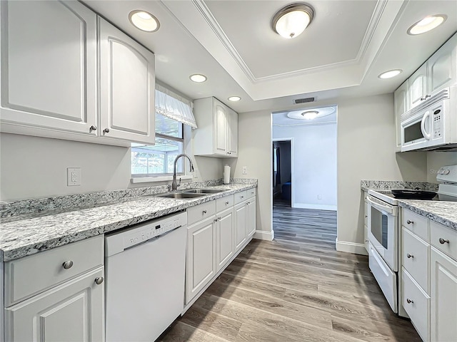 kitchen with white appliances, a raised ceiling, light wood-style flooring, ornamental molding, and a sink