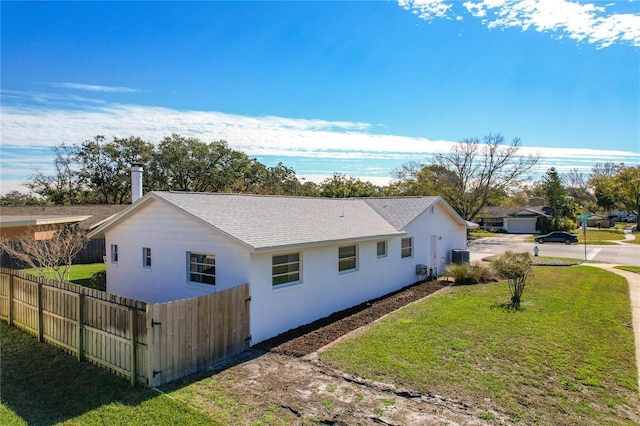 view of side of property featuring a shingled roof, fence, a yard, stucco siding, and a chimney