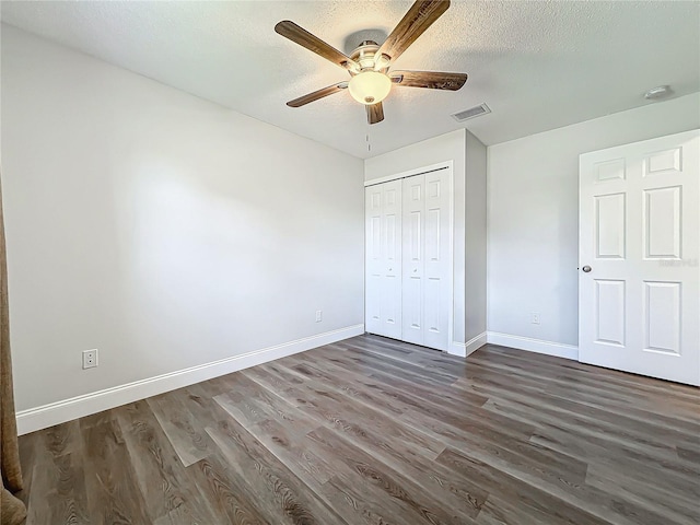 unfurnished bedroom featuring baseboards, visible vents, dark wood finished floors, a textured ceiling, and a closet