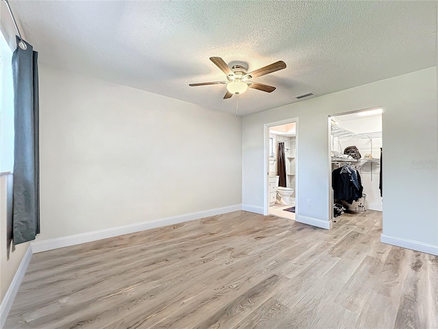 unfurnished bedroom featuring a textured ceiling, light wood-type flooring, a walk in closet, and baseboards