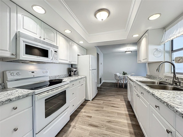 kitchen featuring white appliances, crown molding, a raised ceiling, and a sink