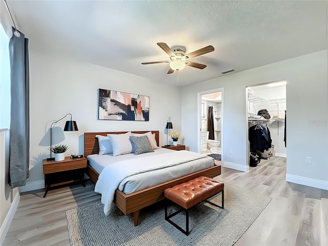 bedroom featuring light wood finished floors, visible vents, baseboards, a walk in closet, and a textured ceiling