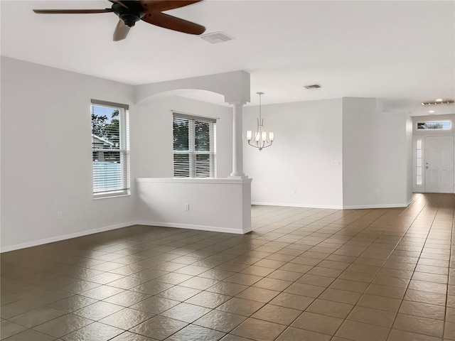 spare room with dark tile patterned floors, ceiling fan with notable chandelier, and decorative columns