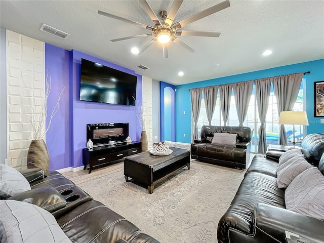 living room featuring ceiling fan, light hardwood / wood-style flooring, and a textured ceiling