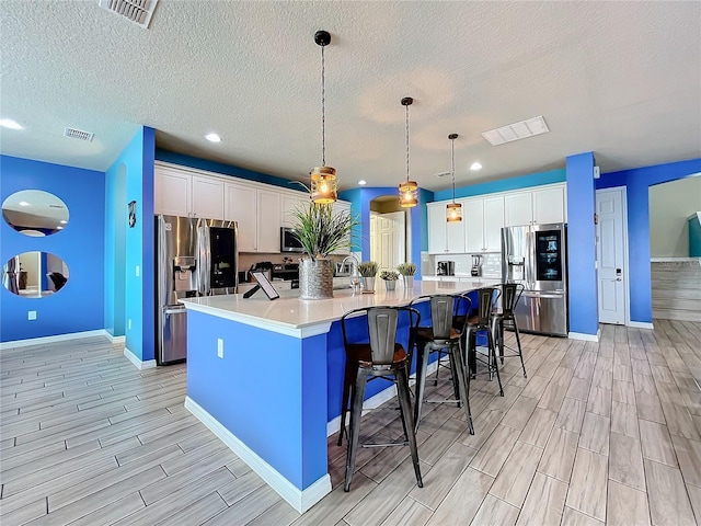 kitchen with a spacious island, appliances with stainless steel finishes, decorative light fixtures, white cabinetry, and a kitchen breakfast bar