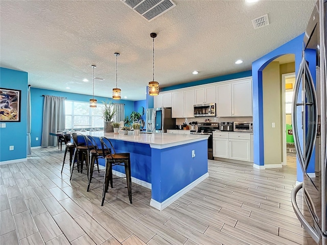 kitchen with appliances with stainless steel finishes, decorative light fixtures, white cabinetry, a breakfast bar, and a center island with sink