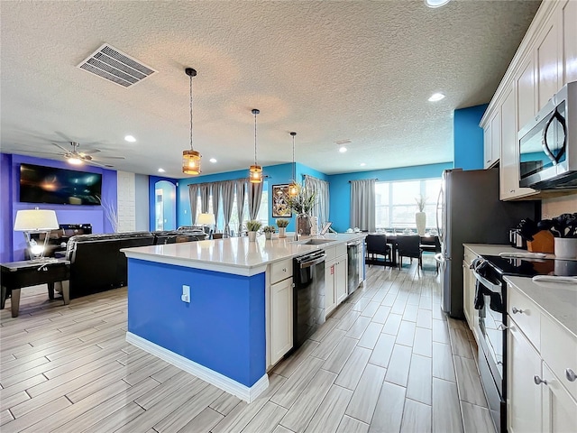 kitchen featuring a textured ceiling, appliances with stainless steel finishes, white cabinetry, hanging light fixtures, and a center island with sink