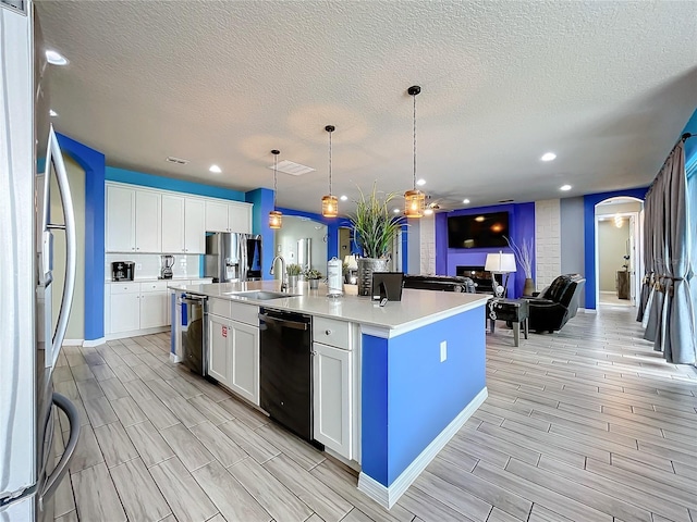 kitchen featuring sink, white cabinetry, black dishwasher, a center island with sink, and stainless steel refrigerator