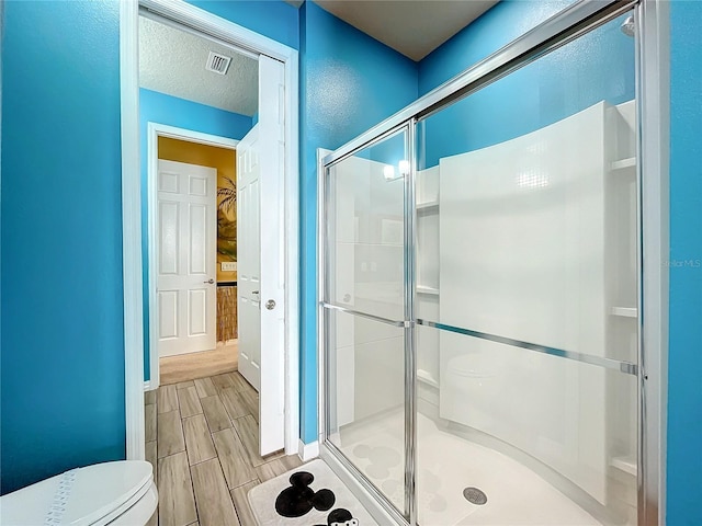 bathroom featuring a textured ceiling, toilet, and a shower with shower door