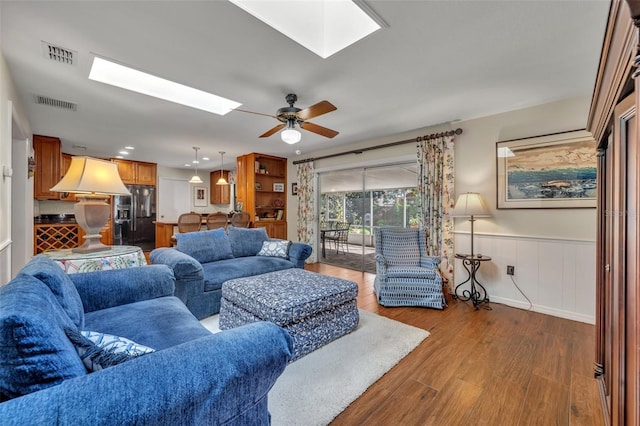 living room featuring hardwood / wood-style floors, ceiling fan, and a skylight