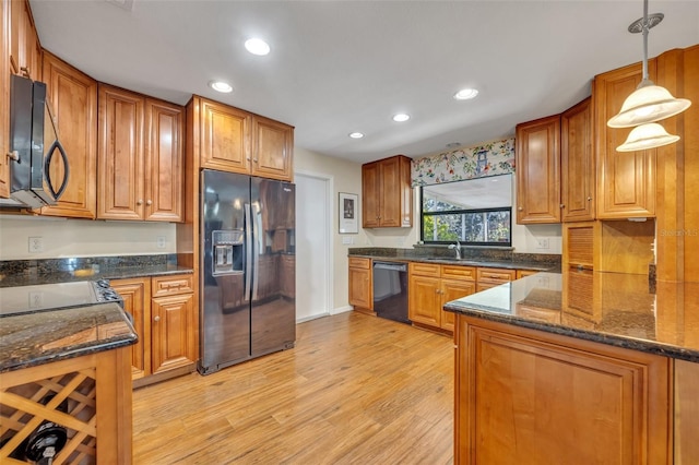 kitchen featuring pendant lighting, sink, dark stone countertops, black appliances, and light wood-type flooring