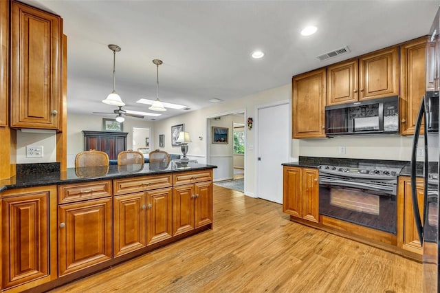 kitchen featuring dark stone countertops, hanging light fixtures, black appliances, kitchen peninsula, and light wood-type flooring