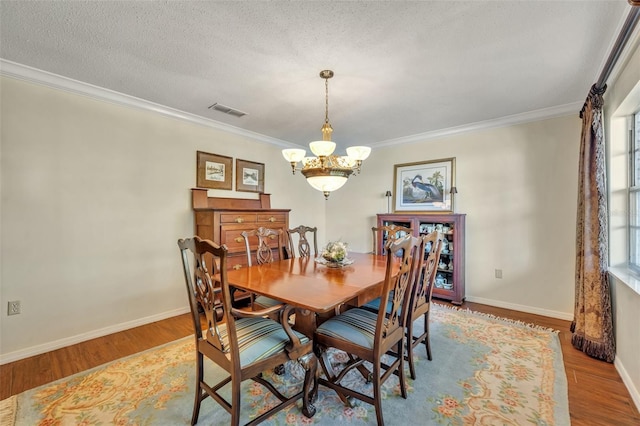 dining room featuring crown molding, wood-type flooring, a textured ceiling, and a notable chandelier