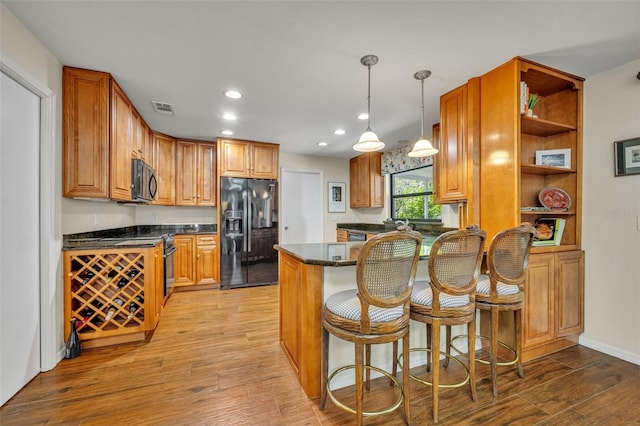 kitchen with hanging light fixtures, a breakfast bar area, light wood-type flooring, and black appliances