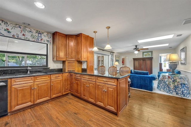 kitchen with pendant lighting, a skylight, sink, dark stone counters, and kitchen peninsula