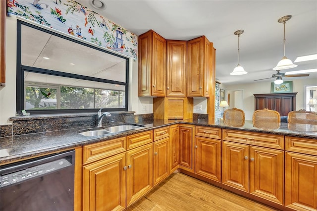 kitchen featuring sink, black dishwasher, decorative light fixtures, dark stone counters, and light wood-type flooring