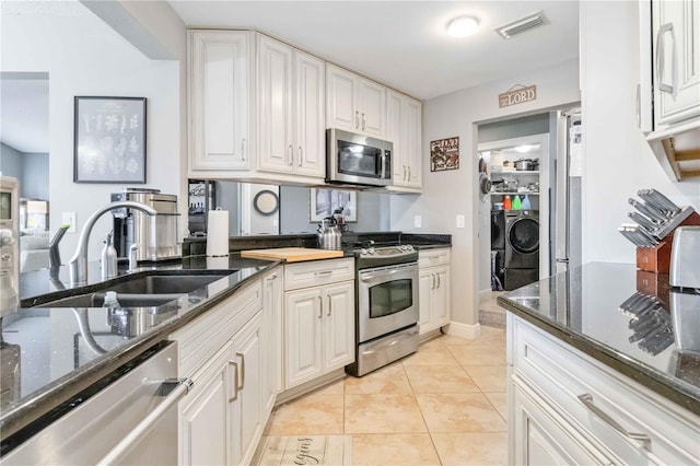 kitchen featuring light tile patterned floors, white cabinets, sink, washer and dryer, and stainless steel appliances