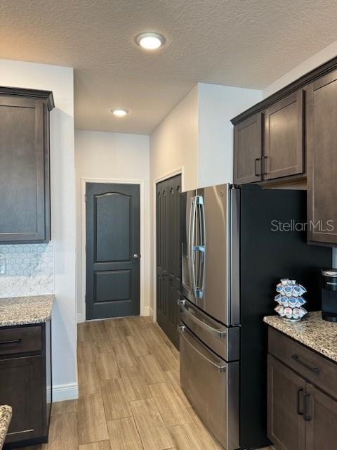 kitchen with light stone countertops, light wood-type flooring, stainless steel fridge, and dark brown cabinetry