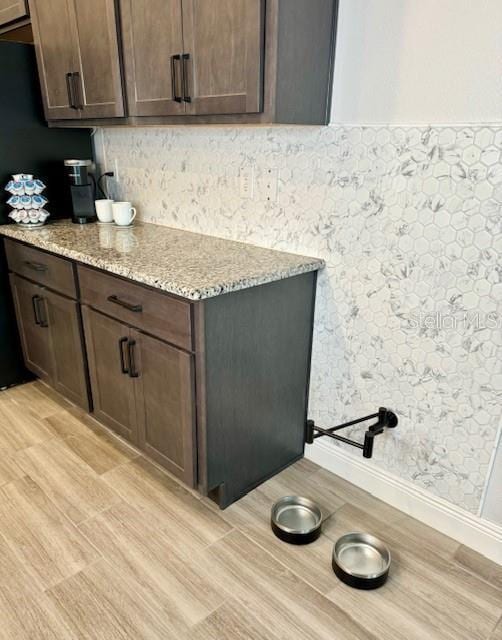 kitchen featuring dark brown cabinetry, light stone counters, and light wood-type flooring