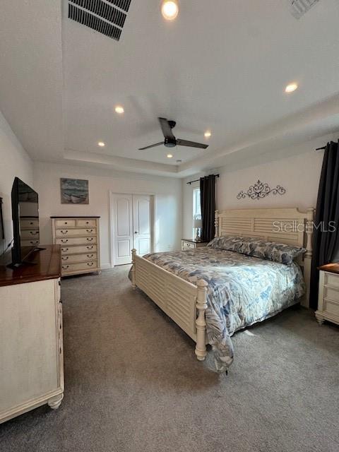 carpeted bedroom with a tray ceiling and ceiling fan