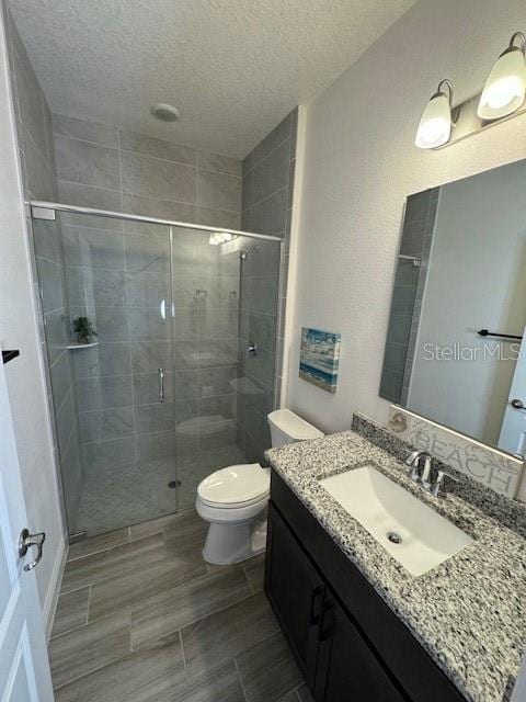 bathroom featuring vanity, toilet, a textured ceiling, and a shower with shower door