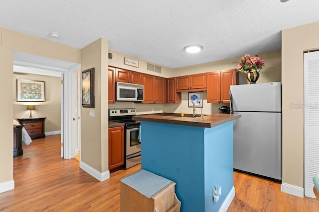 kitchen with sink, a center island with sink, a textured ceiling, appliances with stainless steel finishes, and light hardwood / wood-style floors