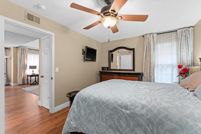 bedroom with ceiling fan, light hardwood / wood-style floors, and a textured ceiling