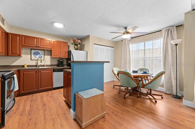 kitchen with sink, a textured ceiling, a kitchen island, stainless steel appliances, and light hardwood / wood-style floors