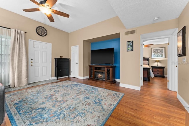 living room featuring hardwood / wood-style flooring, ceiling fan, and a textured ceiling